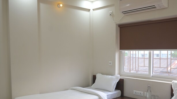 Hotelkamer met twee bedden, een plafondventilator, een airconditioner, een raam met uitzicht en een nachtkastje met een fles en glazen.