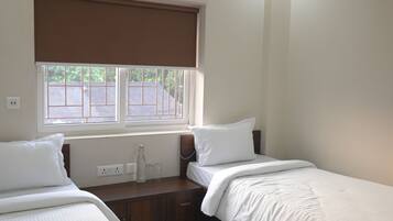 Hotelkamer met twee bedden, een raam met zonwering, een airconditioning en een nachtkastje met een fles en glazen.