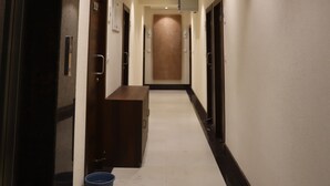 Een hotelgang met een receptiebalie, deuren en een blauwe prullenbak.