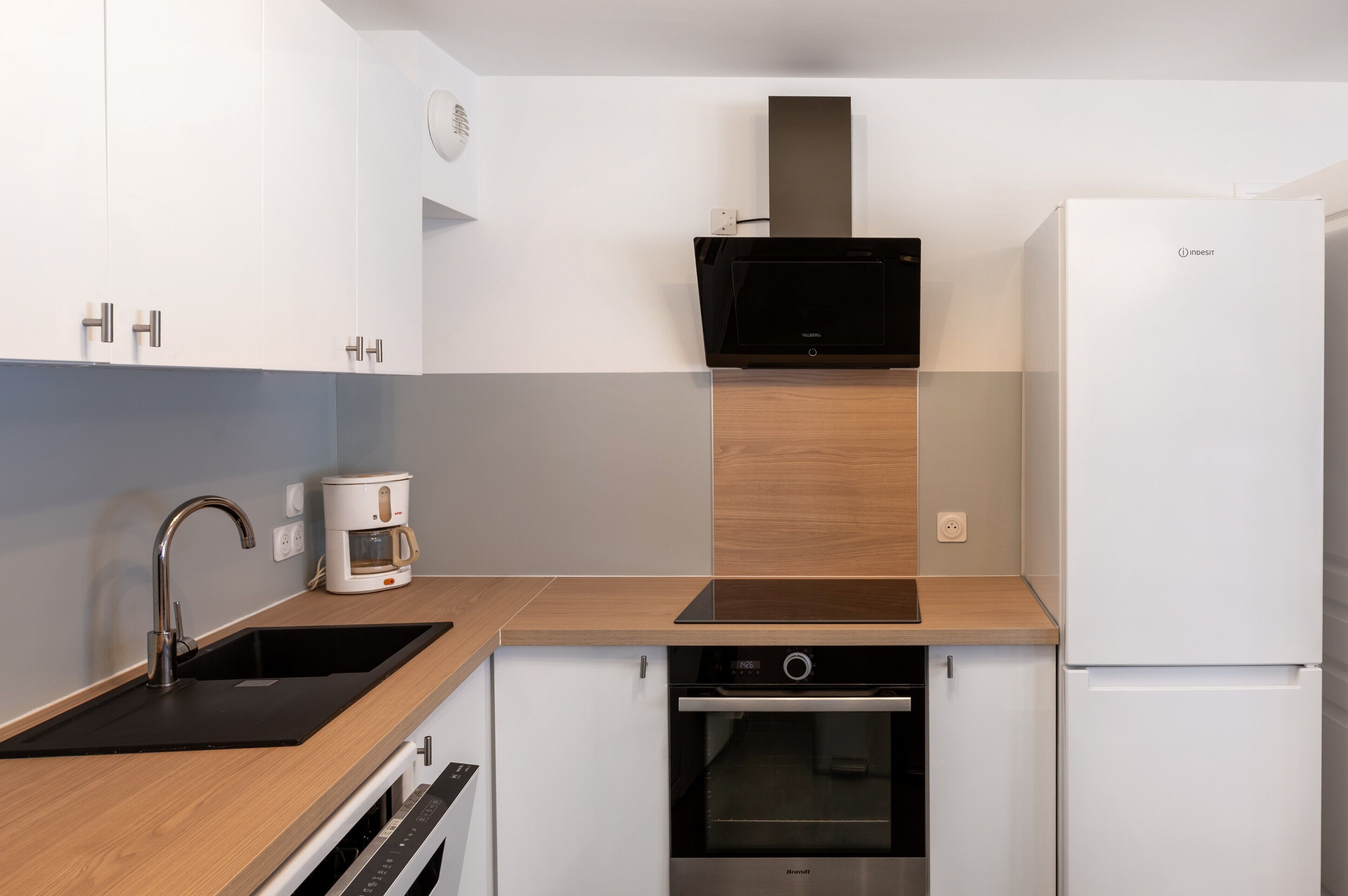 Een moderne keuken met een inbouwoven, een koffiezetapparaat en een witte koelkast.