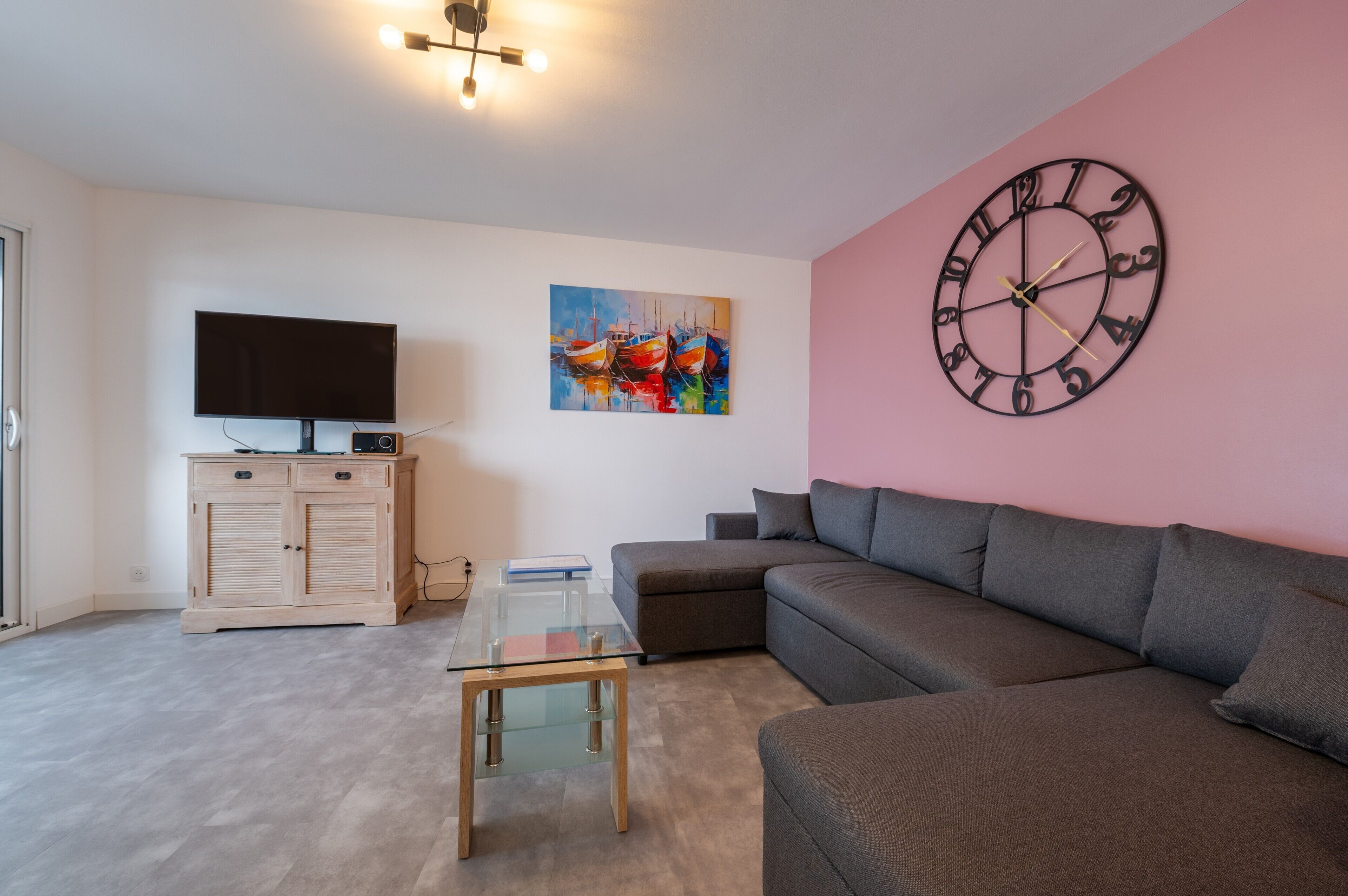 Una sala de estar con sofá, televisión, mesa de centro de vidrio, aparador y un reloj de pared.