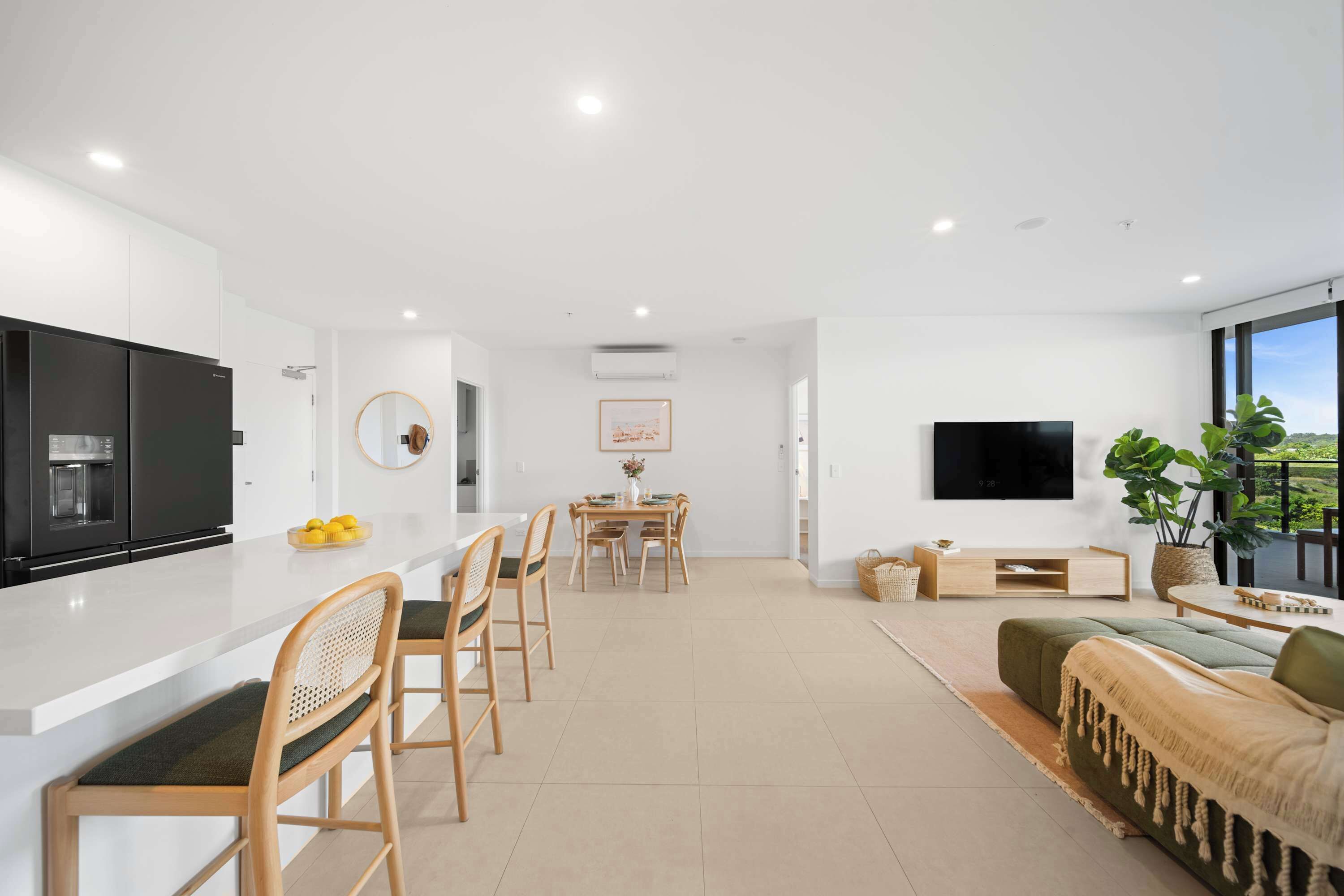 A modern kitchen with a dining area, a flat-screen TV, and a large window offering a view.