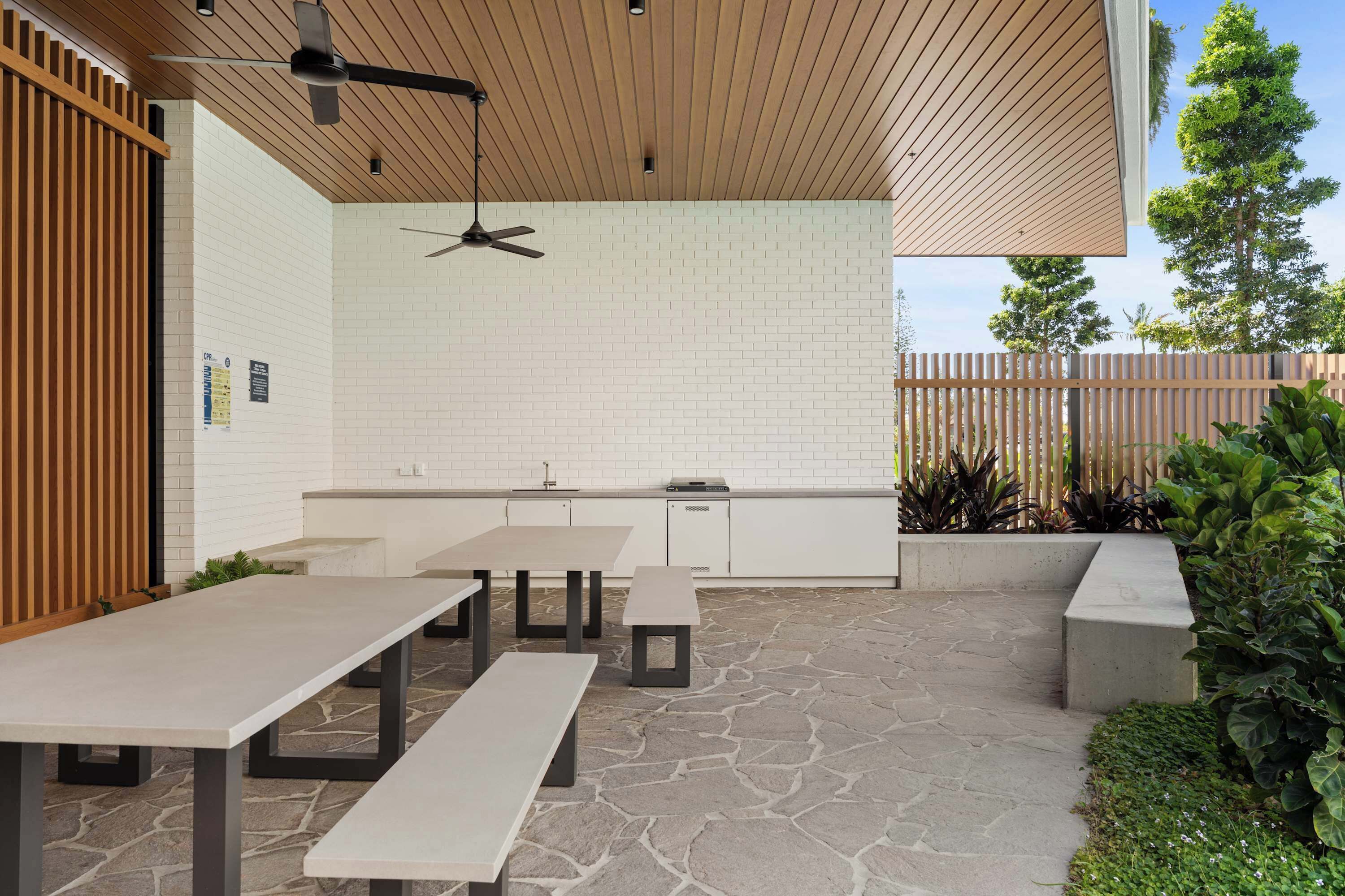 An outdoor patio area with stone flooring, a wooden ceiling, and a white brick wall.