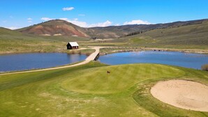 Ein Golfplatz mit Teich, Scheune und sanften Hügeln im Hintergrund.