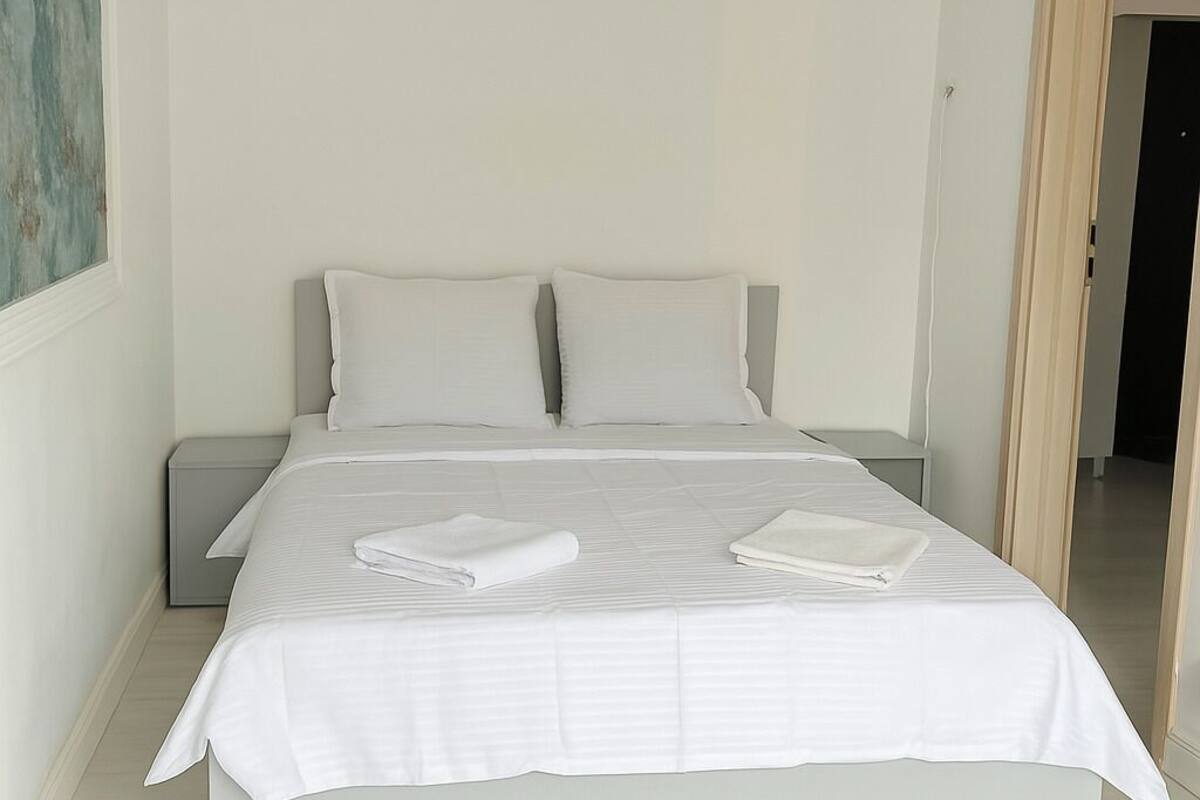 A modern bedroom with a large bed, two pillows, a nightstand, and a painting on the wall.