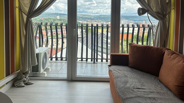 A balcony with a view of a cityscape, a sofa, and a table.