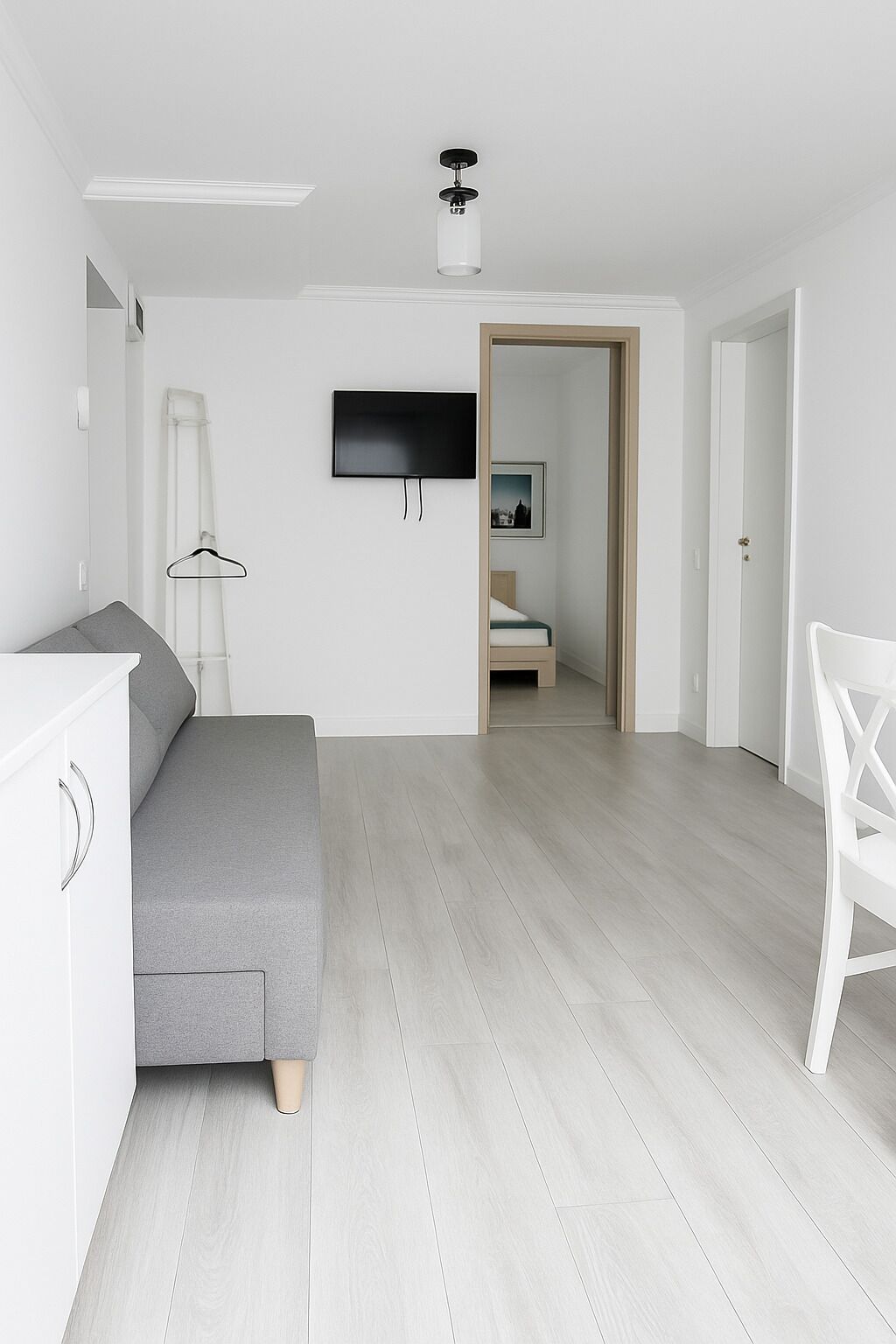 A modern, minimalist bedroom with a grey sofa, a flat-screen TV, and a wooden door leading to another room.
