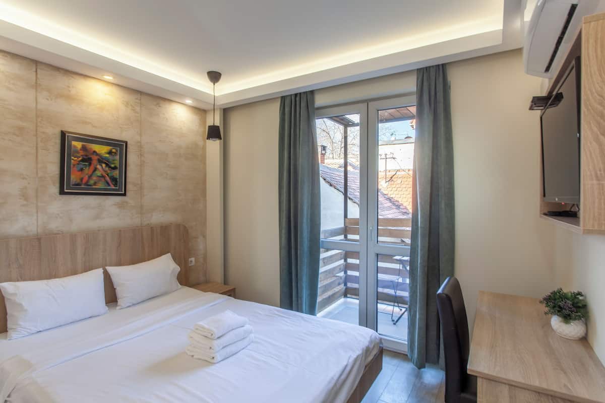 Een hotelkamer met een bed, een bureau, een stoel, een televisie en een balkon met uitzicht.