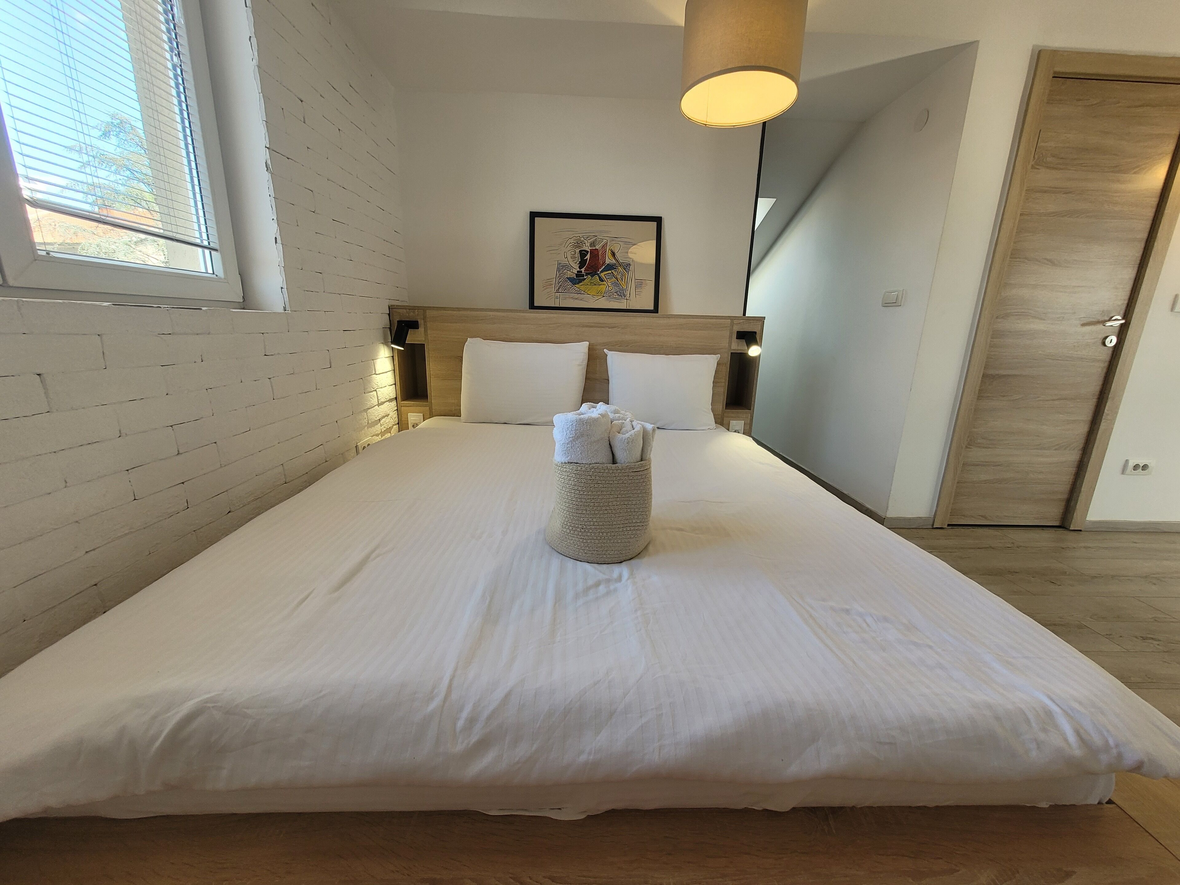 A neatly made bed with white linens, a headboard, and a bedside lamp.