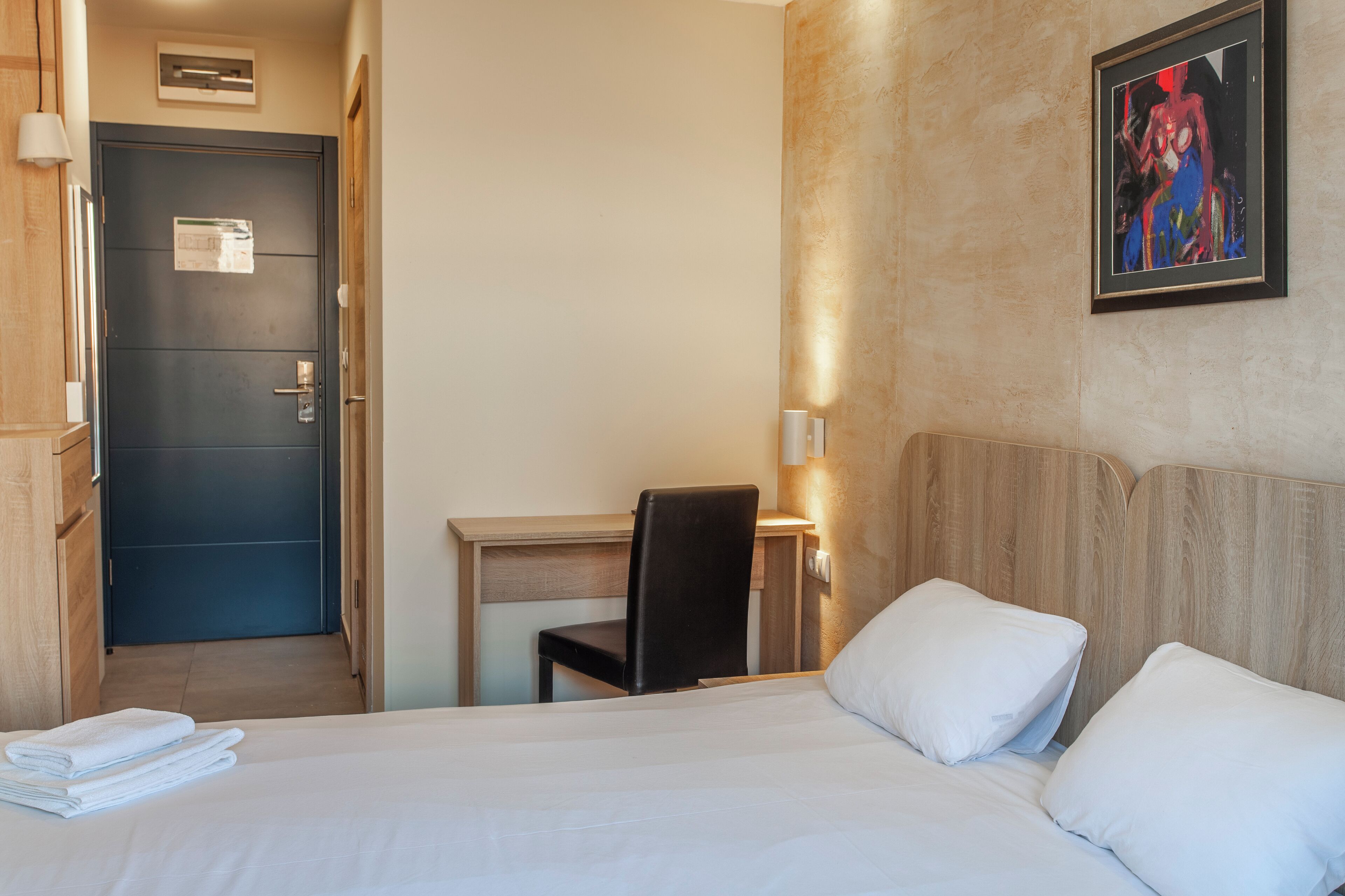 Quarto de hotel com cama, escrivaninha, cadeira e um quadro na parede.