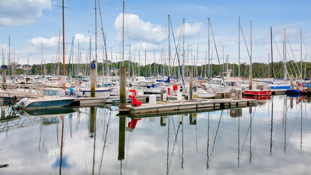 Un port de plaisance où sont amarrés de nombreux bateaux, l’eau est calme et le ciel est dégagé.