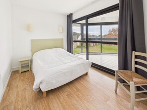 A bedroom with a bed, a nightstand, a chair, a large window, and a view of the outdoors.