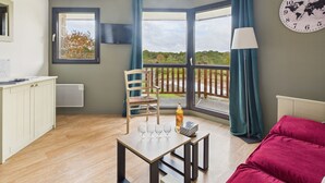 Une pièce moderne comprenant une table à manger, des chaises, un canapé rouge, une horloge en forme de carte du monde, et une vue sur une rivière et la verdure environnante.