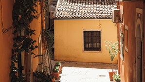 Une ruelle étroite avec un toit recouvert de tuiles, des plantes en pot et une petite fenêtre.