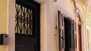 Un bâtiment jaune avec une porte et des volets noirs, une petite fenêtre et un lampadaire.