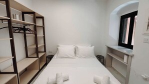 Une chambre à coucher avec un lit, deux oreillers, une fenêtre et des étagères intégrées où sont suspendus des vêtements.