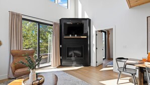 A modern living room with a fireplace, a dining area, and large windows offering a view of trees. - Sevierville Retreat • Indoor Pool + Hot Tub + Firepit + Gym | Ridgeview Retreat (Sevierville)