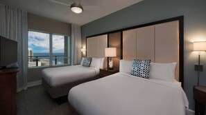 Ett hotellrum med två sängar, ett stort fönster med utsikt över staden, en takfläkt och en TV som står på ett stativ.