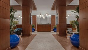 Zona de recepción con mostrador de madera, dos jarrones azules, sillas de mimbre e iluminación colgante.