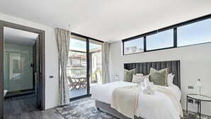 Una habitación de hotel moderna con una cama grande, cabina de ducha de vidrio y balcón con vistas a la ciudad.