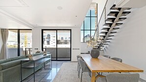 Una sala de estar moderna con un sofá, una mesa de comedor y sillas. Se observa una escalera con un diseño original en la pared.