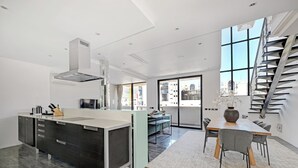 Una cocina moderna con una isla central, un comedor con mesa y sillas, y una escalera que conduce a un nivel superior.