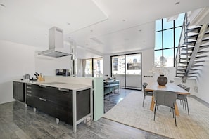 A modern kitchen with a central island, a dining area with a table and chairs, and a staircase leading to an upper level.
