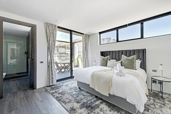 A modern bedroom with a large bed, a glass door leading to a balcony, and a city view.