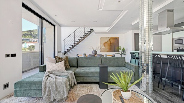 Una sala moderna con sofá verde, una escalera y una zona de cocina.