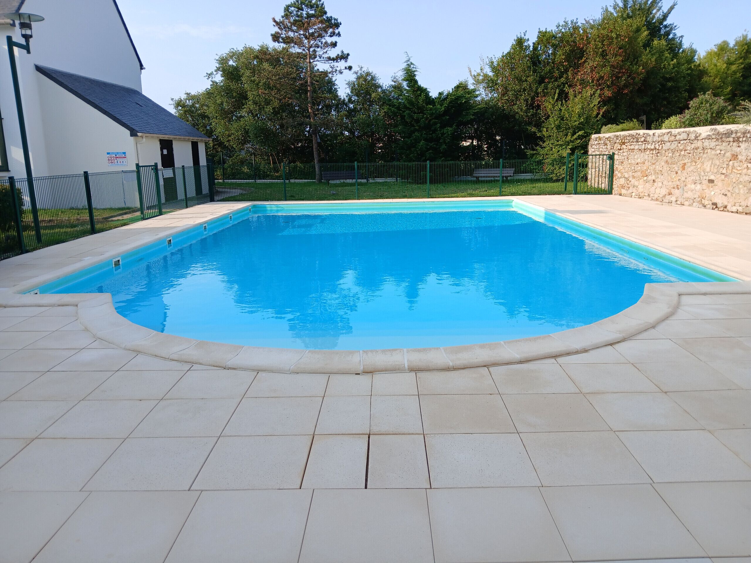 Una piscina rettangolare con bordo piastrellato, circondata da un muro in pietra e una recinzione.