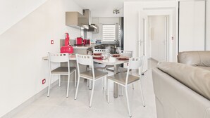 A modern kitchen with white cabinetry, a red coffee machine, and a dining area with white chairs and a table set for two. - House in residence, pool, 2 adults/2 children (Le Croisic)