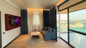 A modern living room with a large window, a sofa, a round coffee table, and a flat-screen TV mounted on the wall. - Khorazm Hotel (Tashkent)