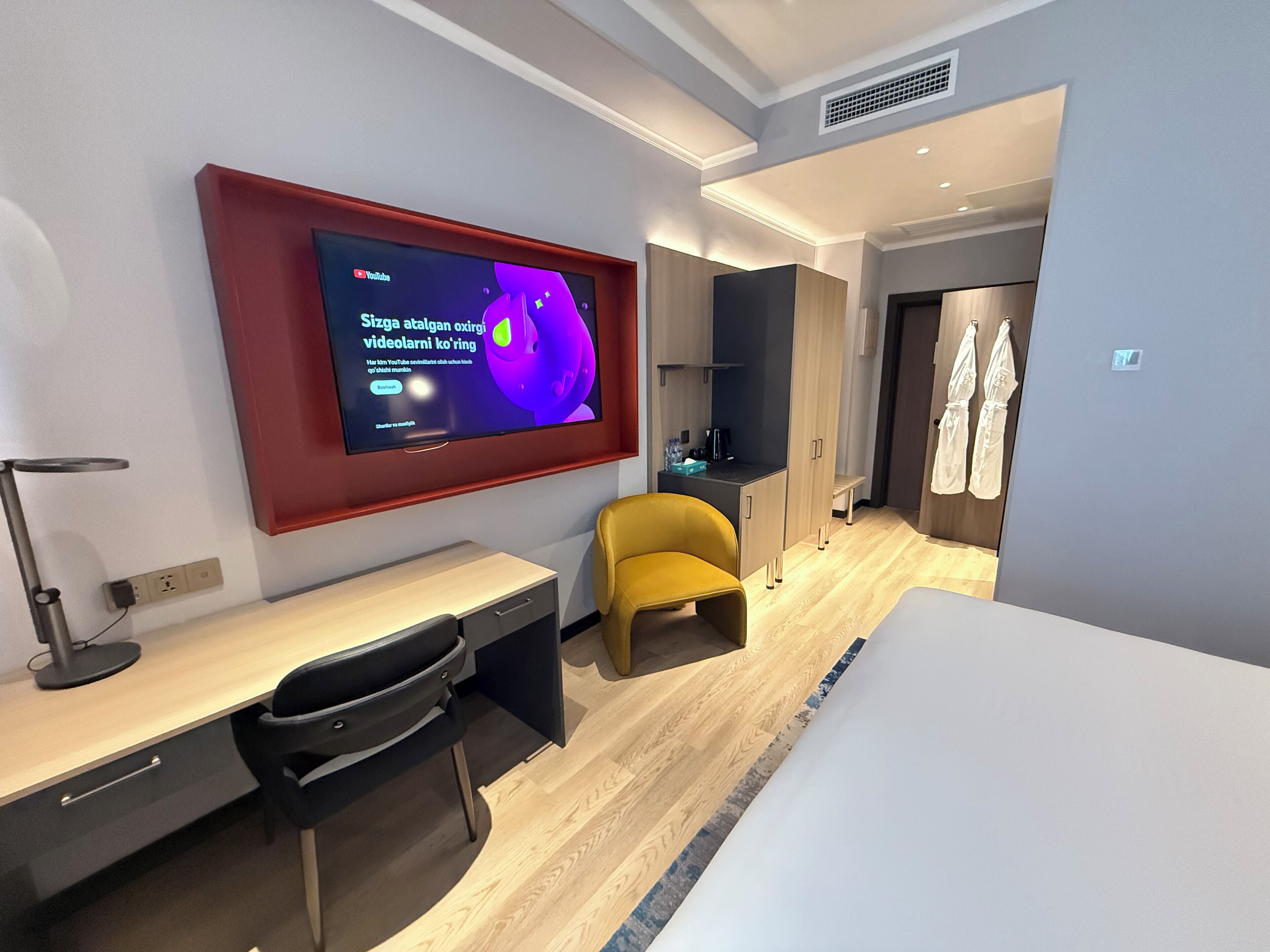 Habitació d'hotel amb escriptori, cadira, llit, televisió penjada a la paret i armari.