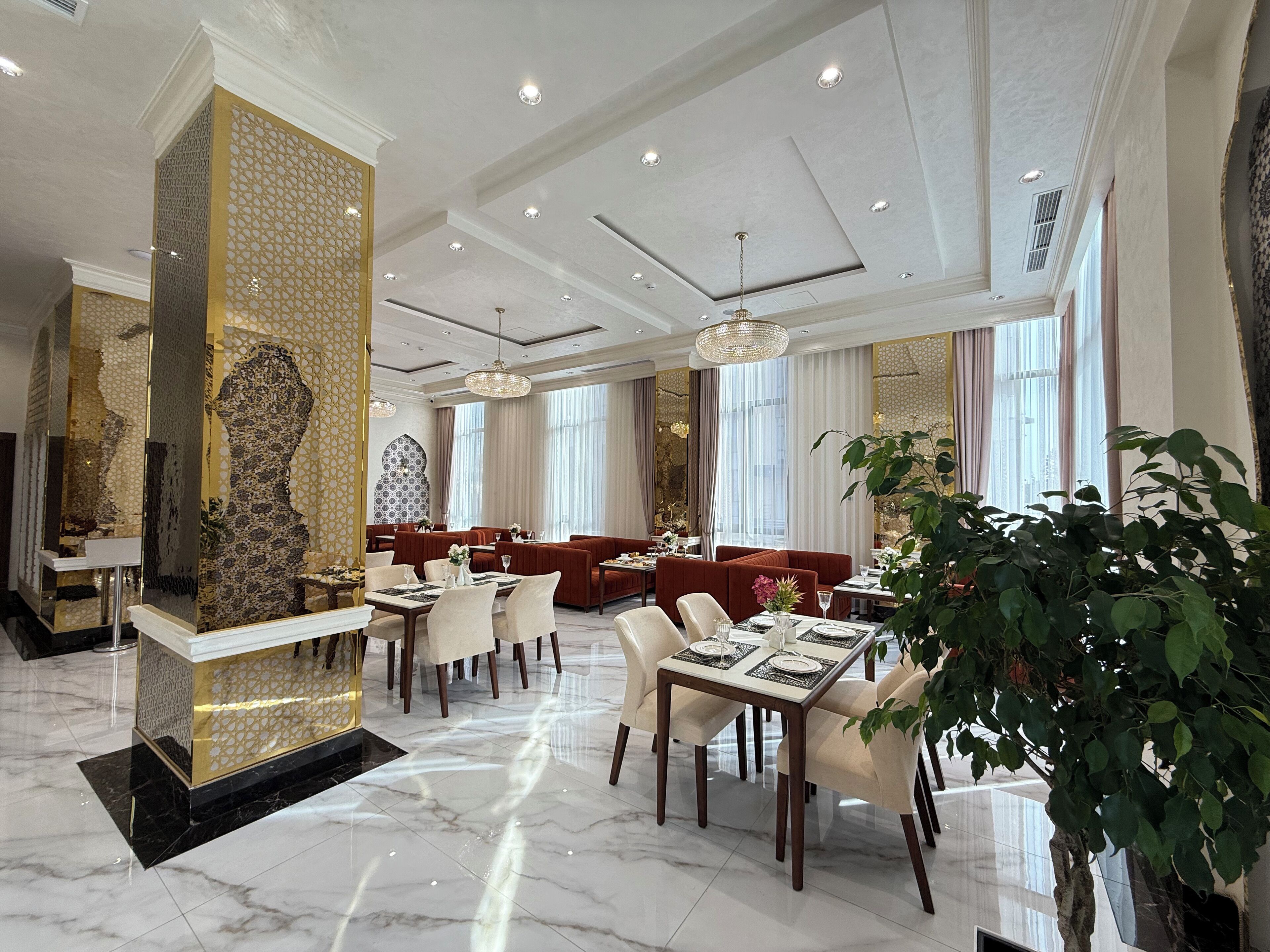 En rymlig hotellobby med marmorgolv, röda sittmöbler och en stor, dekorativ skulptur.