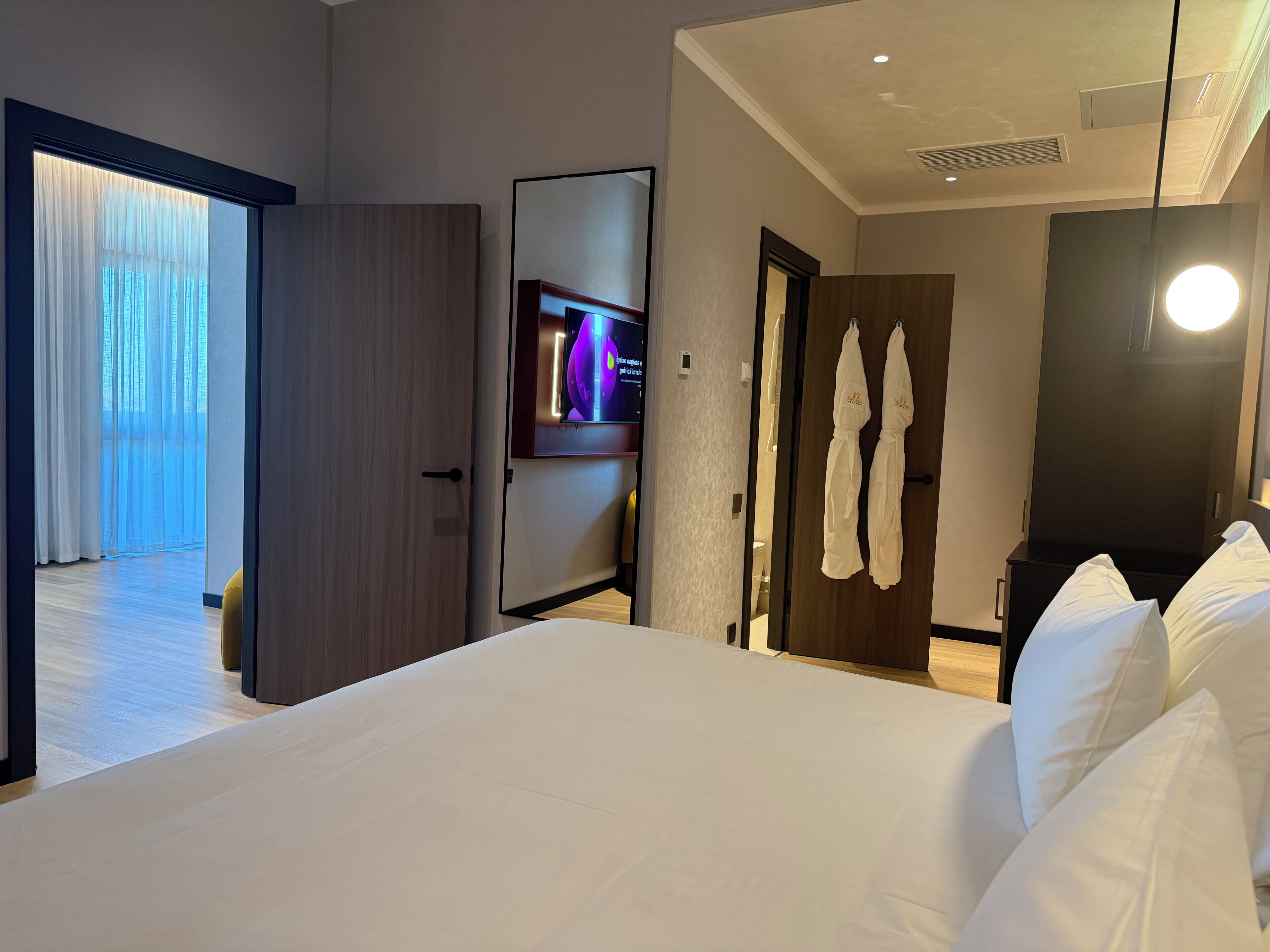 Ein Hotelzimmer mit einem großen Bett, einem an der Wand befestigten Fernseher und einer Tür zu einem Balkon.