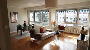 A modern living room with a sofa, dining table, chairs, and large windows.