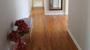A hallway with wooden flooring, white walls, and a door leading to another room.