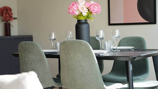 A dining table set with four chairs, a vase with flowers, and wine glasses.