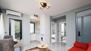 Una sala de estar moderna con un sofá, una mesa de centro y un comedor. Se observa una cocina al fondo con lavadora y una mesa de comedor.