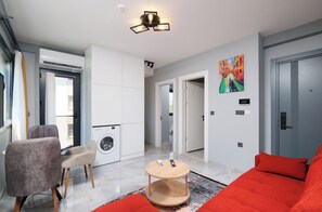 A modern living room with a red sofa, a round wooden coffee table, and a washing machine in the background. - Q'in Homes (Fethiye)