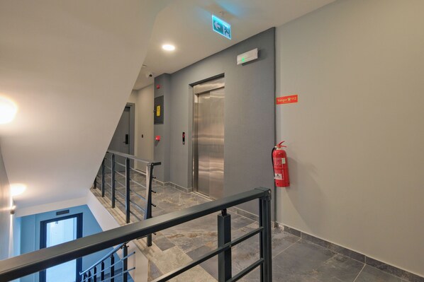 A modern hotel interior with a staircase, an elevator, and a fire extinguisher.