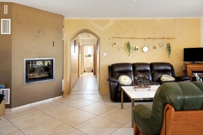 Ein Wohnzimmer mit Kamin, Fernseher und einer Sitzecke mit Sofa und Sesseln.