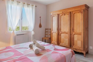 A bedroom with a bed, a wooden wardrobe, a chair, and a window with curtains.