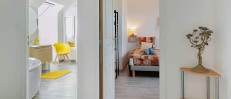 A hotel room with a bed, a bedside table, a lamp, and a view of the bathroom.