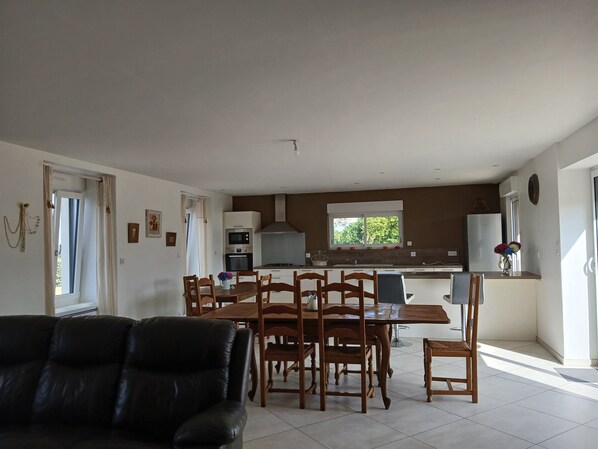 A modern kitchen with a dining area, a black leather sofa, and a window with a view of greenery.