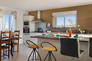 A modern kitchen with a dining area, featuring a large window, a built-in oven, and a dining set with stools.