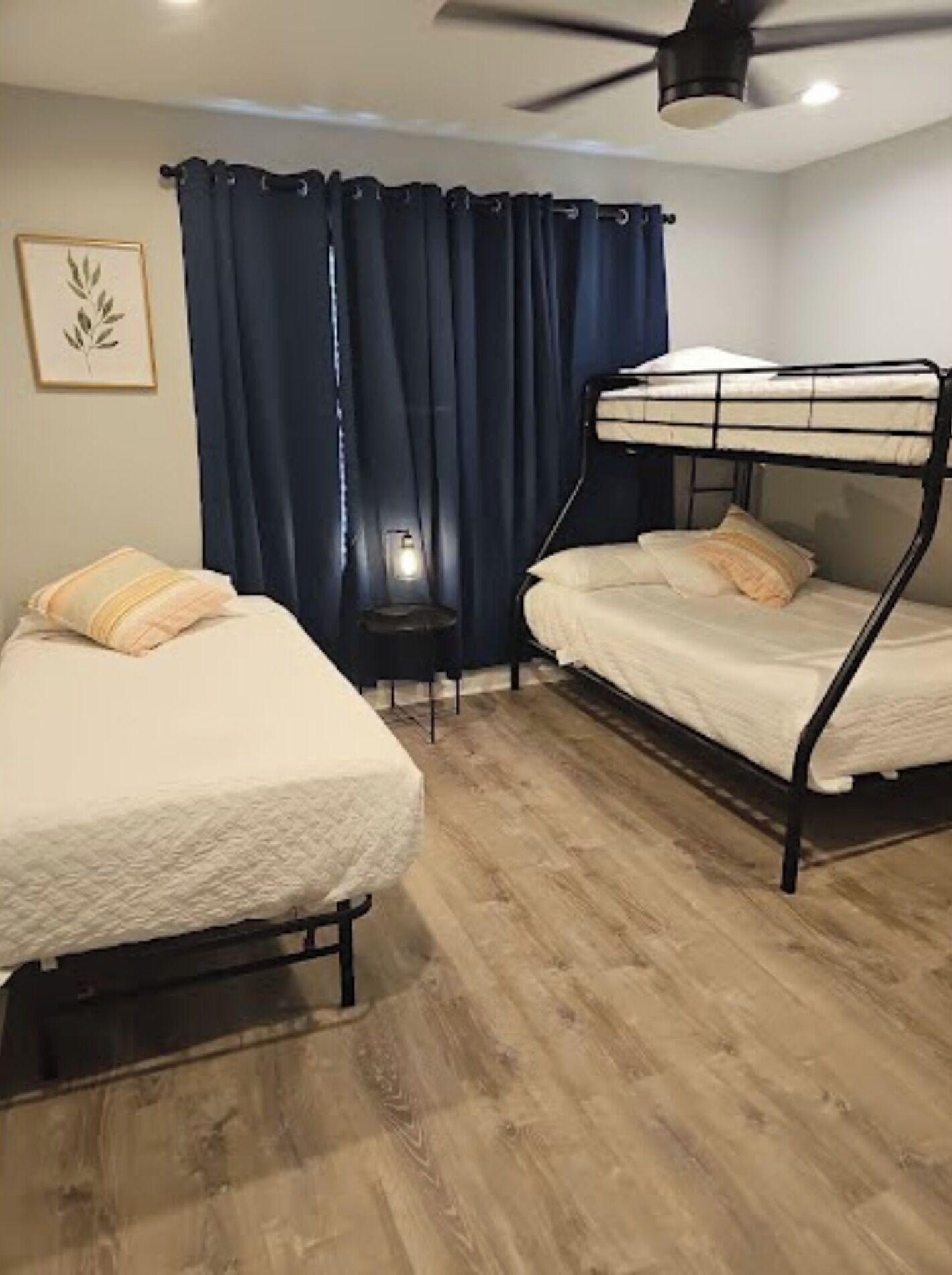 Une chambre avec deux lits superposés, une petite table, une lampe et un ventilateur de plafond.