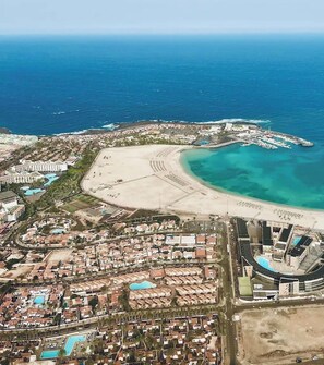 An aerial view of a coastal resort with a beach, a marina, and a large hotel complex.