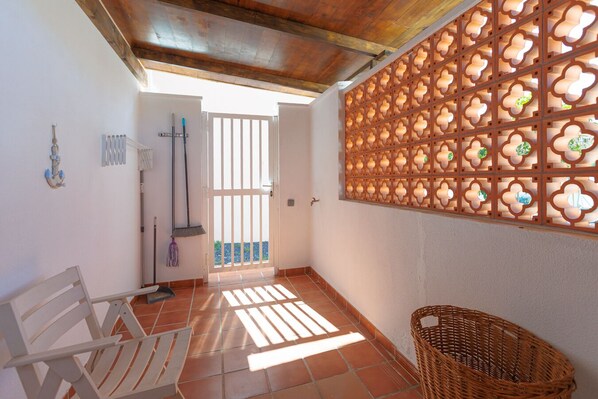 A room with a white bench, a wicker basket, a radiator, a broom, and a decorative wall panel.