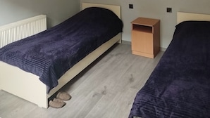 A small, clean room with two single beds, a wooden nightstand, a white radiator, and a simple ceiling light fixture. - Sabir iki (Baku)